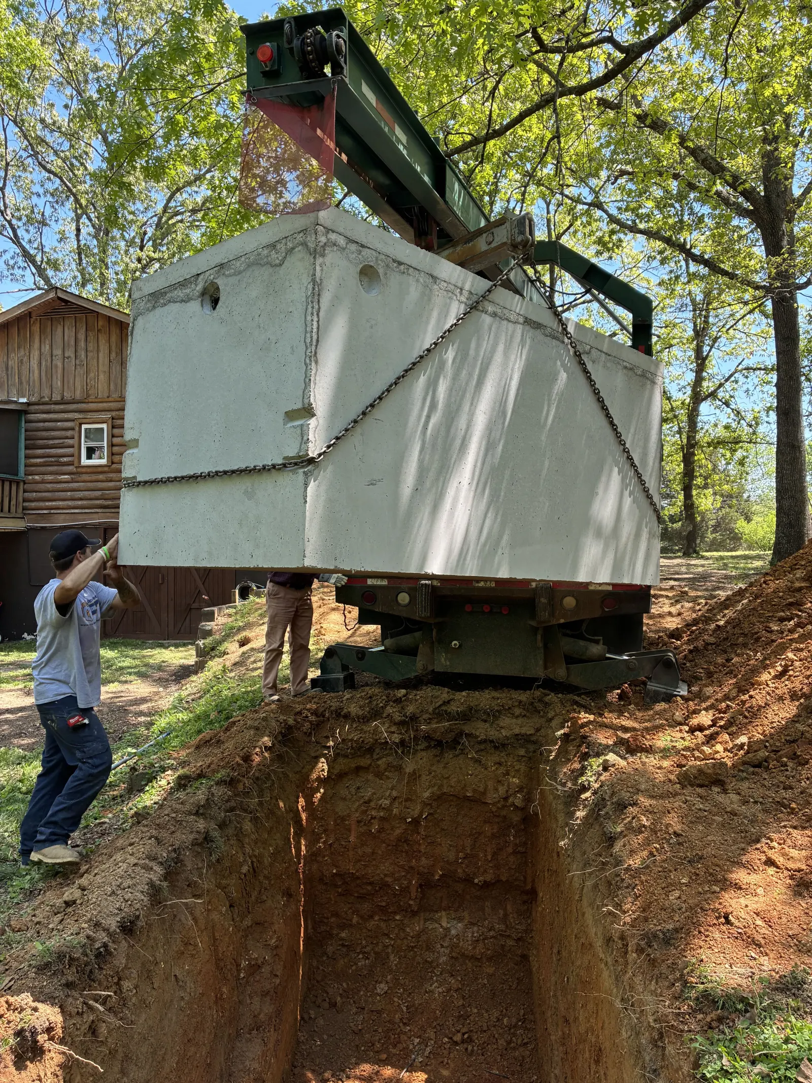 Boom truck lifting a precast septic tank beside a cabin