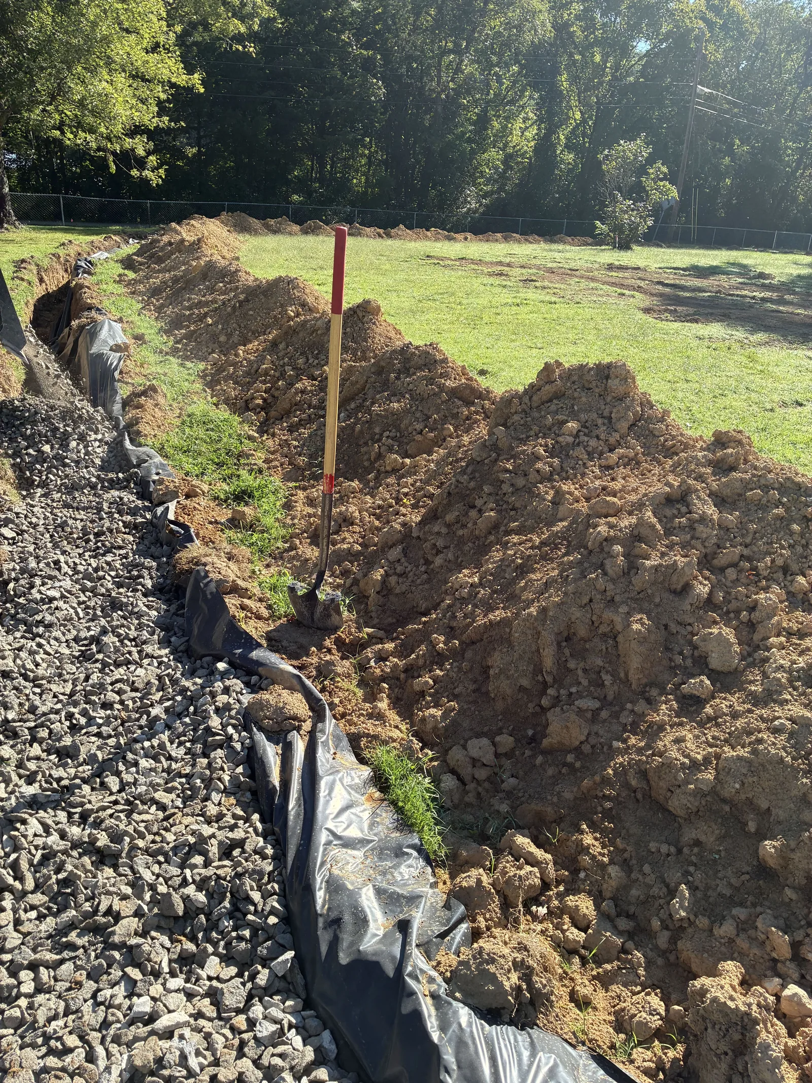 Gravel drain field trench with grade stakes across a lawn