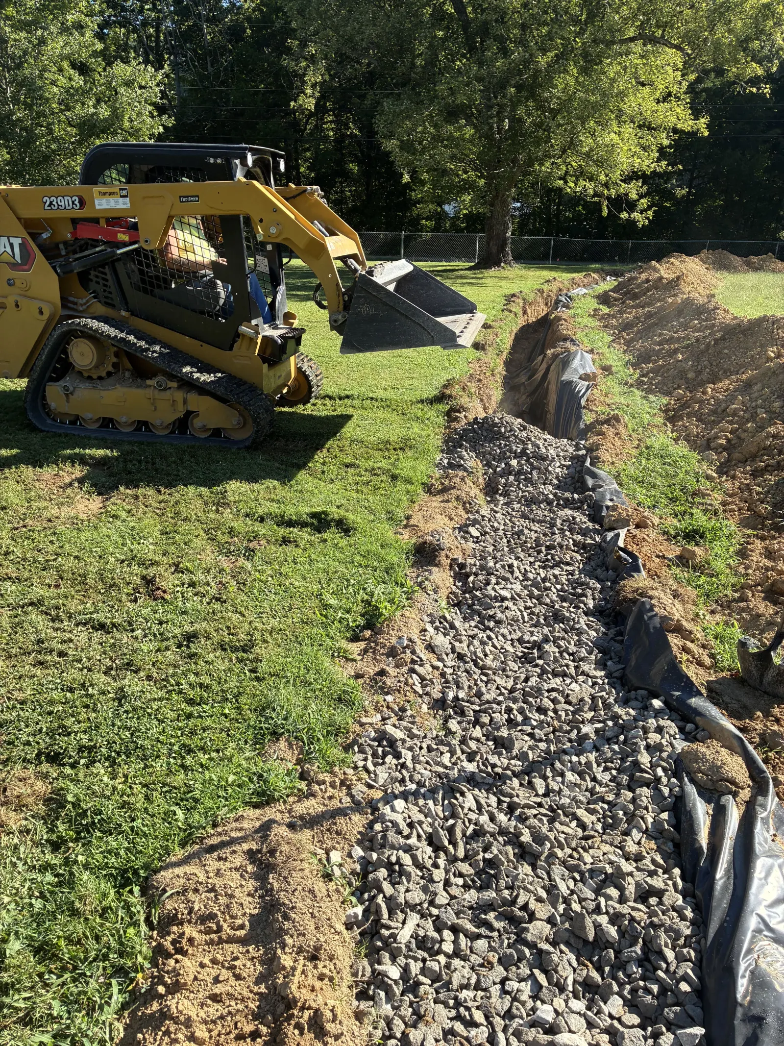 Compact track loader beside a gravel drain field trench lined with fabric