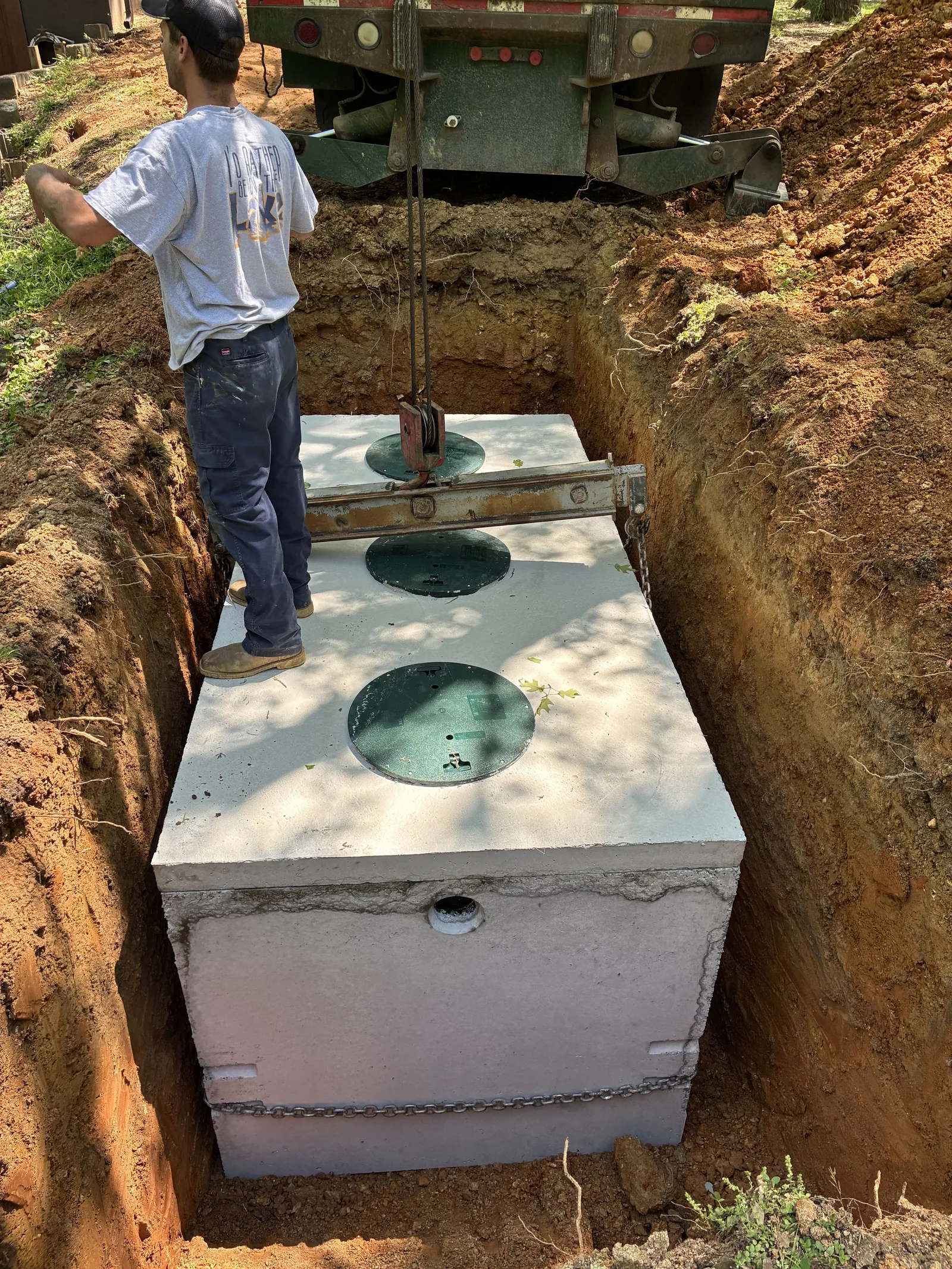 Precast septic tank being guided off the boom truck into the excavation