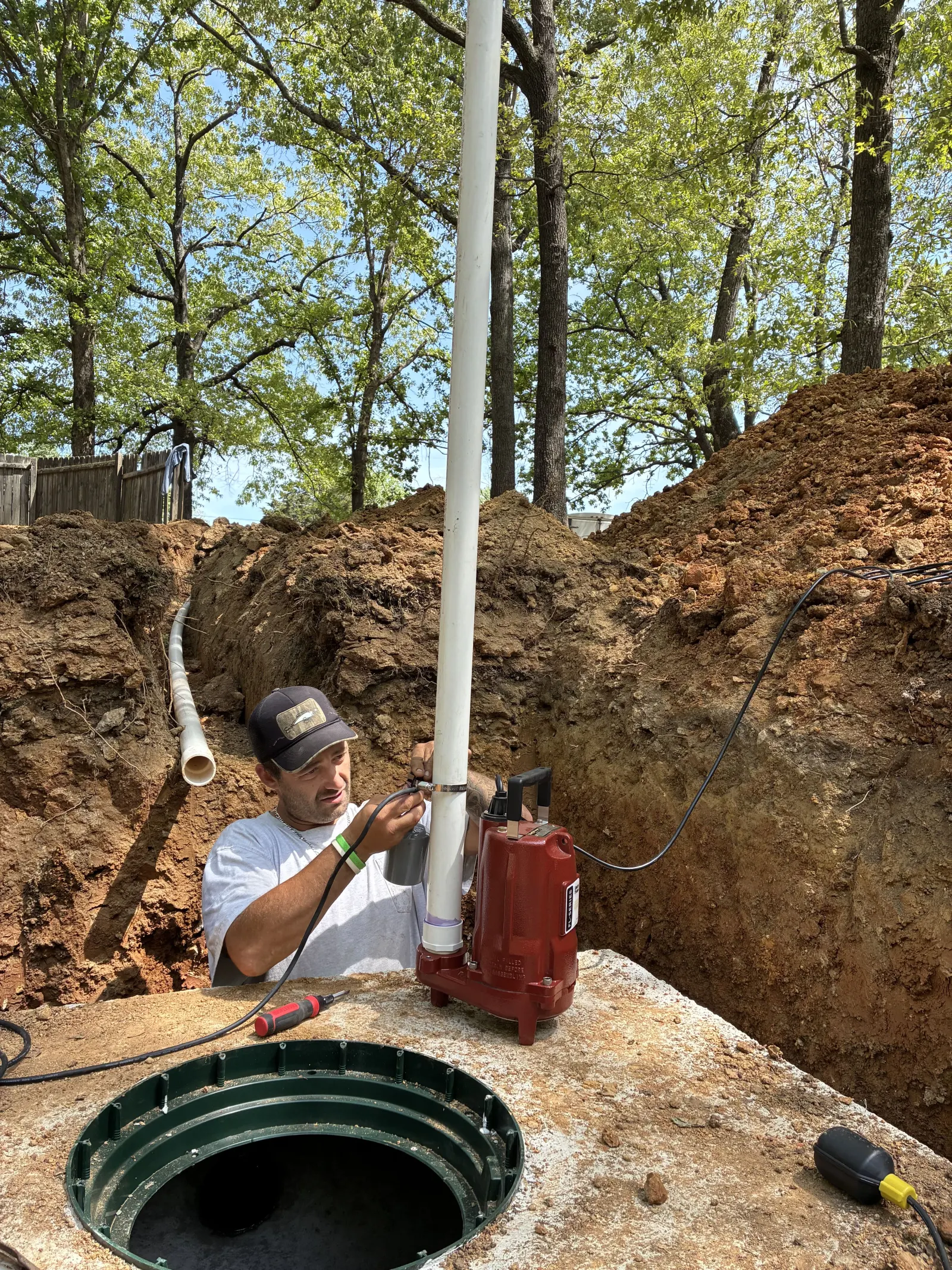 Technician installing a sewage pump on the riser pipe in the trench